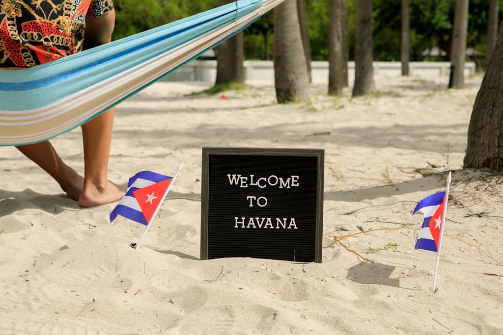 A tropical beach scene featuring a hammock, Cuban flags, and a 'Welcome to Havana' sign.