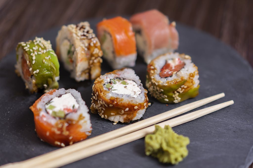 A close-up view of a colorful sushi platter with wasabi and chopsticks on a slate board.