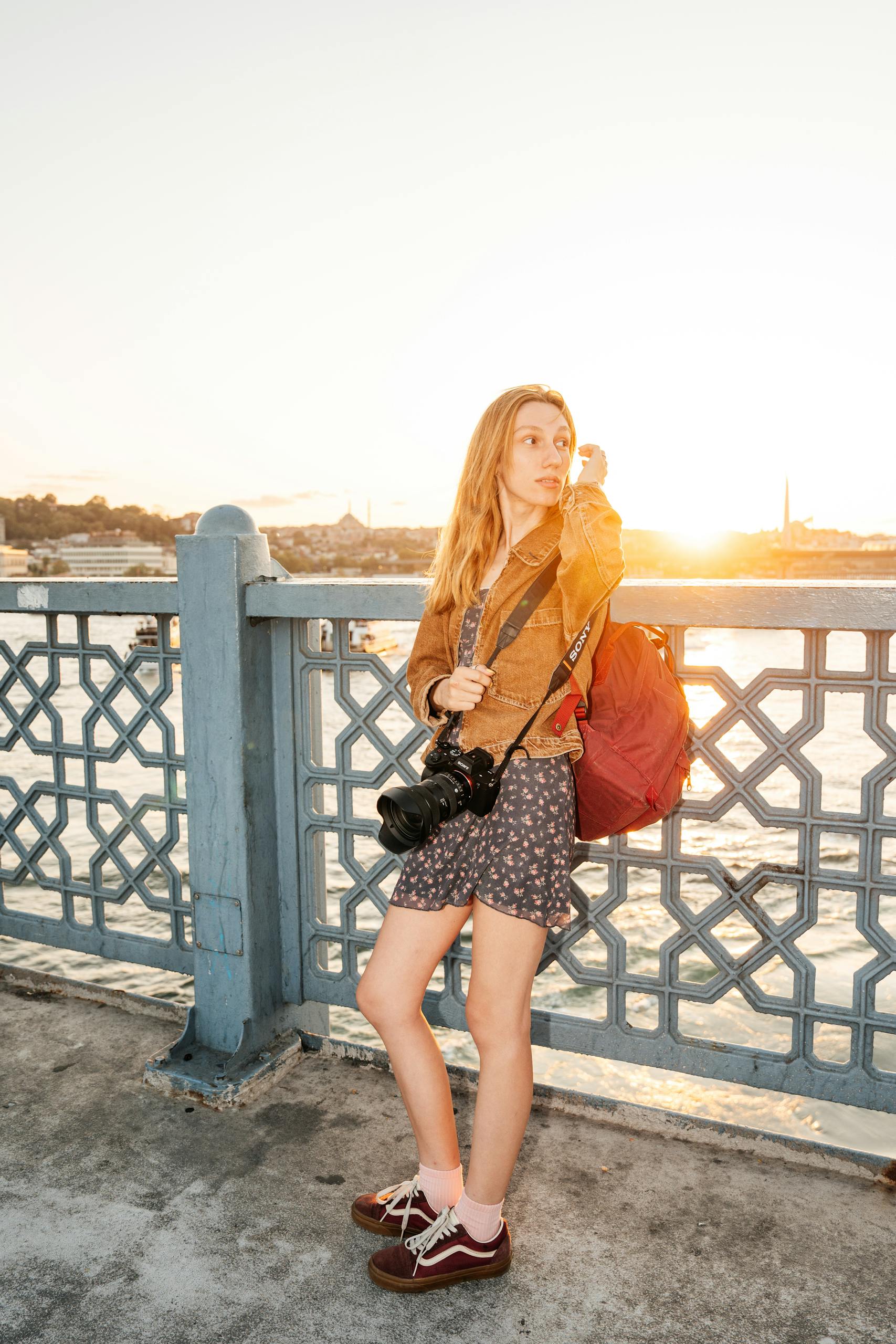 A young woman with a camera enjoys the sunset view on Galata Bridge in Istanbul, Türkiye.