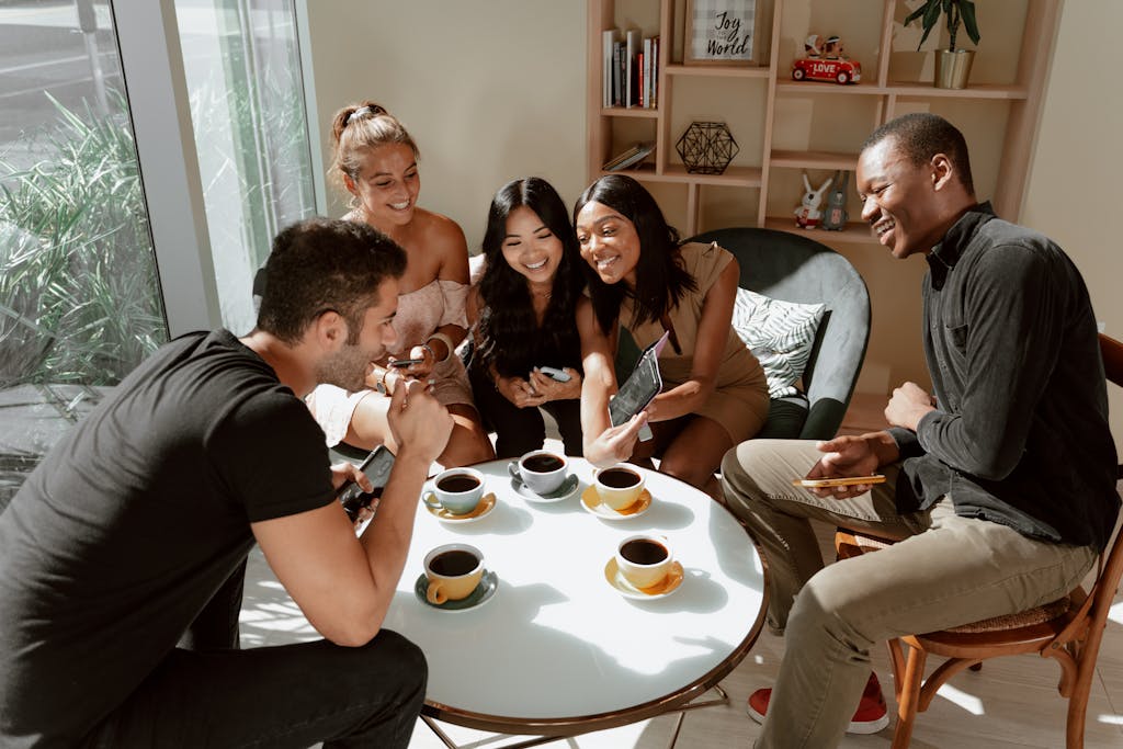 Diverse group of friends laughing and enjoying coffee in a cozy café setting.