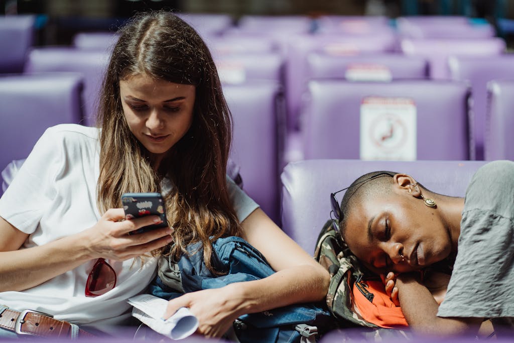 Two young women relaxing in a station. One is texting while the other is resting.