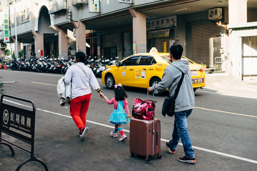 A family walks with luggage past a taxi in Taipei, showcasing urban travel life.