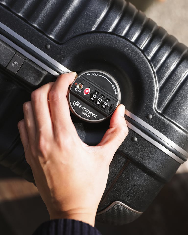 A hand locks a suitcase using a combination lock in a close-up shot, emphasizing security.