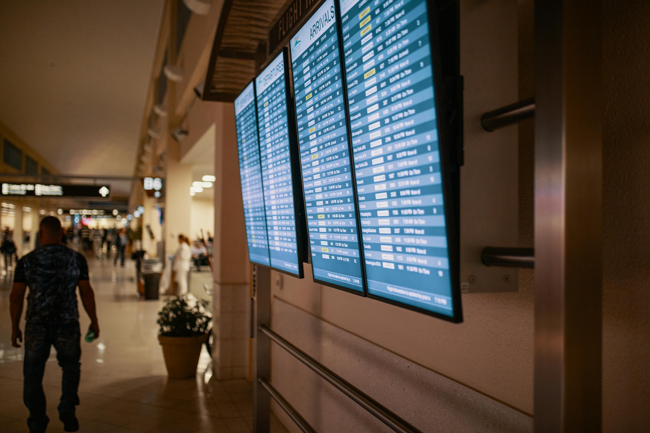Airport terminal with digital flight information boards showing arrivals and departures.