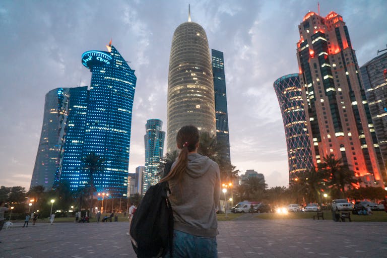 A woman gazes at the illuminated Doha skyline, highlighting modern skyscrapers at twilight.