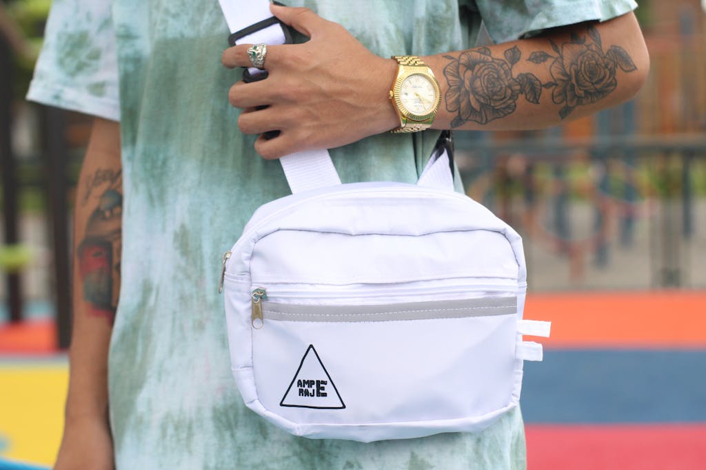 Close-up of a tattooed arm wearing a watch and holding a stylish white sling bag.