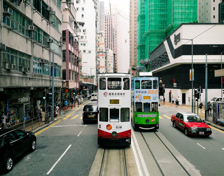 Vibrant double-decker trams navigate a busy street on Hong Kong Island. Iconic urban scene.