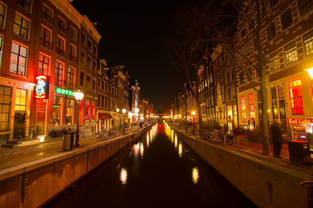 Lively night scene of Amsterdam's canal with illuminated buildings and reflections.
