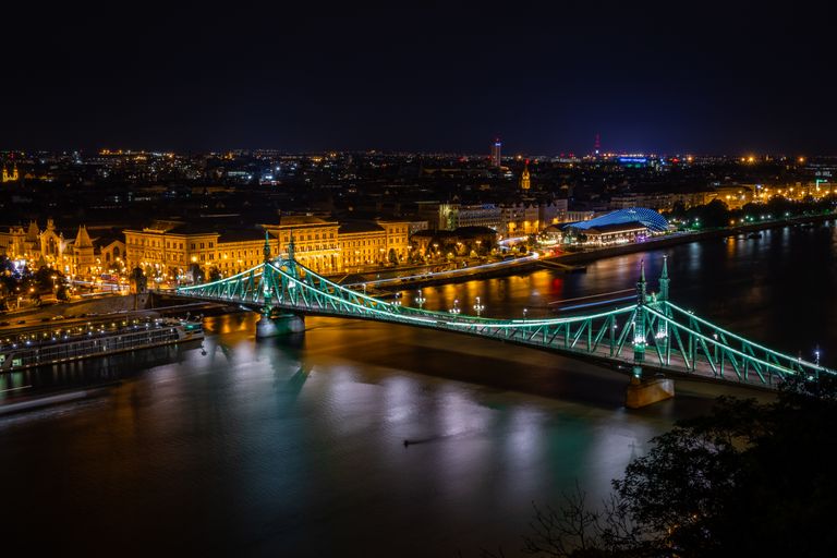 Freedom Bridge in Budapest beautifully lit across the Danube River at night, showcasing the city skyline.
