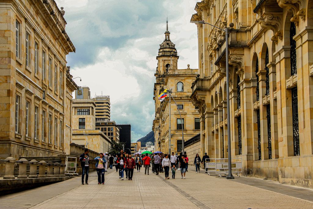 People walking in Bogotá with historic buildings and Colombian flag in view.